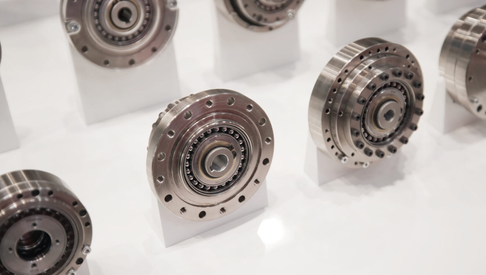 Several metallic precision gears or industrial bearings are displayed upright on white stands, showcased on a glossy white surface.