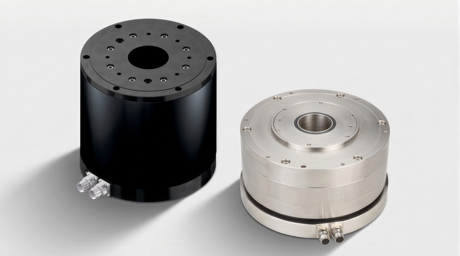 Two cylindrical industrial components, one black and one metallic, each with multiple holes on the top surface and tube connectors at the base, are displayed on a white background.