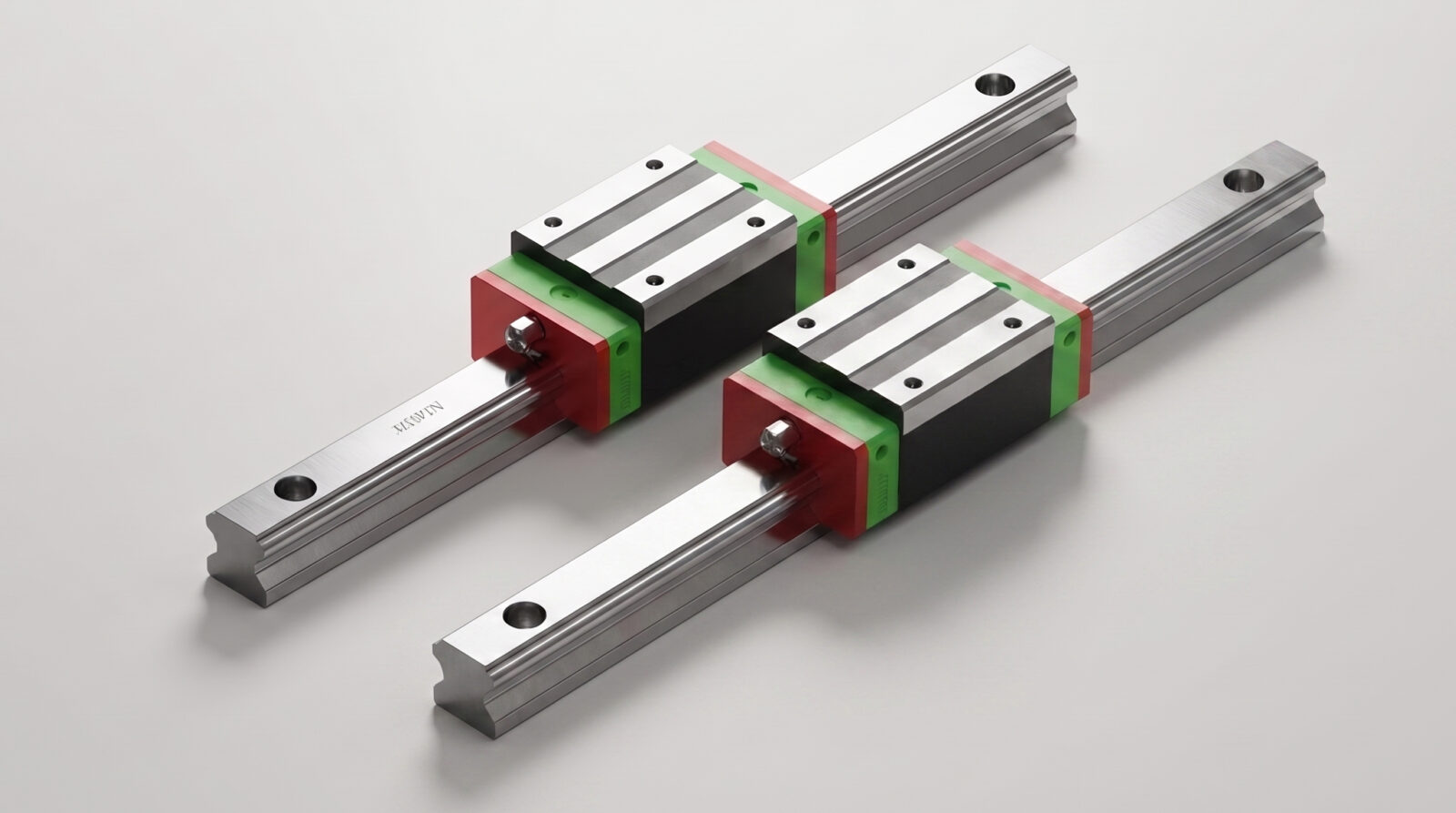 Two metal linear guide rails with green and red sliding blocks are positioned parallel to each other on a light grey surface.