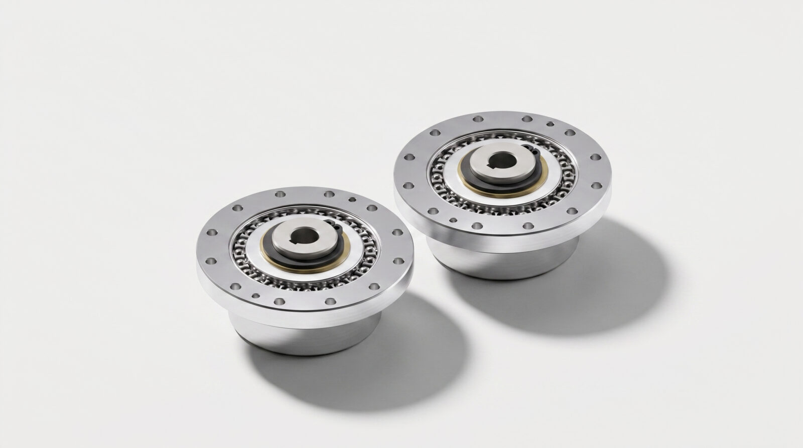 Two shiny metallic circular mechanical components with visible gear teeth, bolts around the edge, and cylindrical bases, placed side by side on a plain white background.