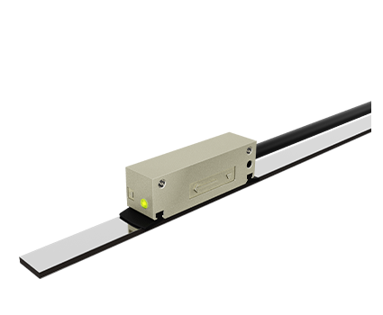 A rectangular metallic sensor with a green indicator light is mounted on a black rail, with a cable attached to the sensor, all set against a plain white background.